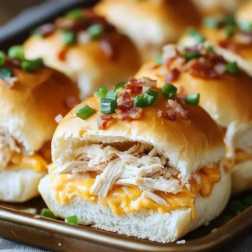 A close-up of a fluffy slider bun filled with shredded chicken, melted cheese, and topped with green onions and bacon bits.