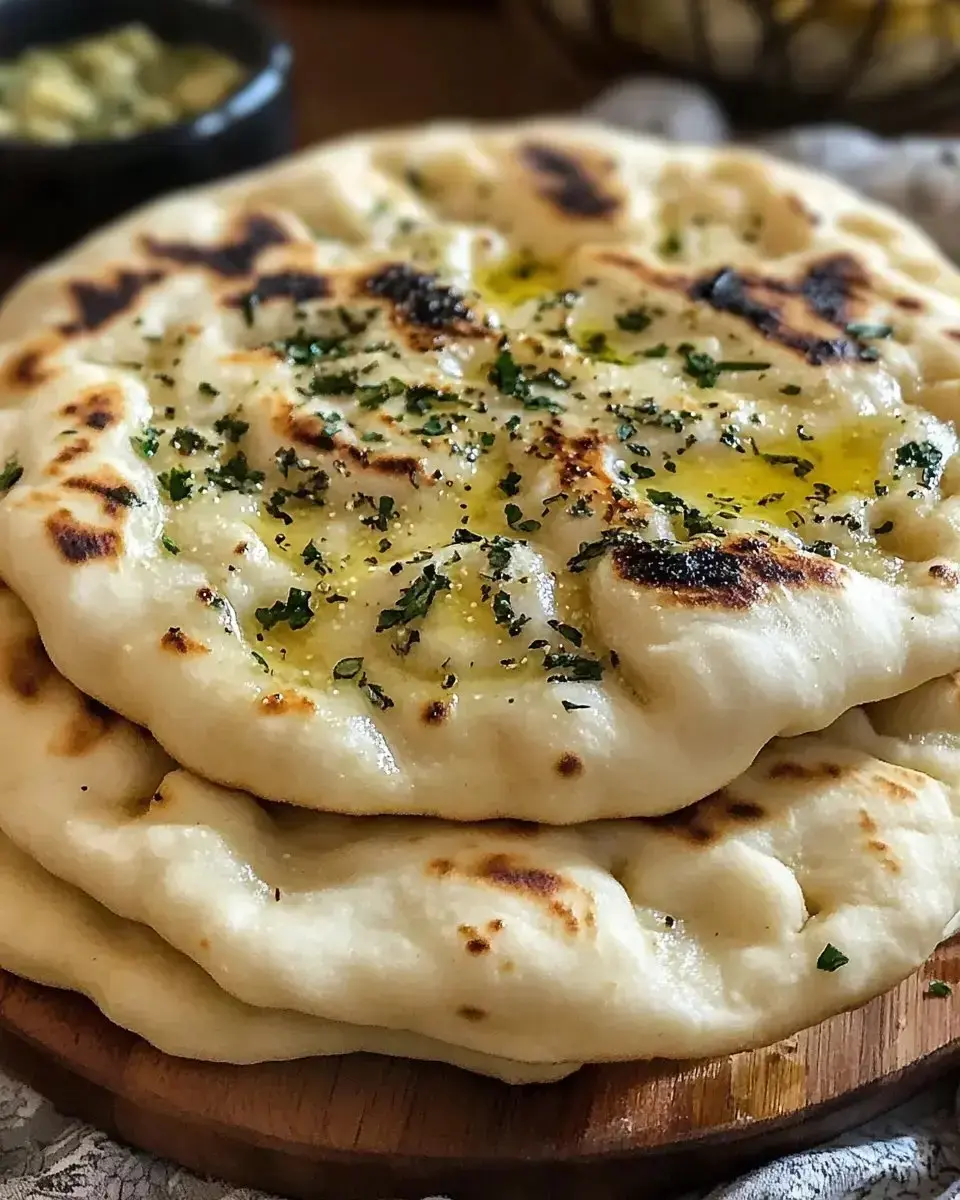 Three pieces of freshly baked naan bread topped with herbs and drizzled with olive oil, placed on a wooden board.