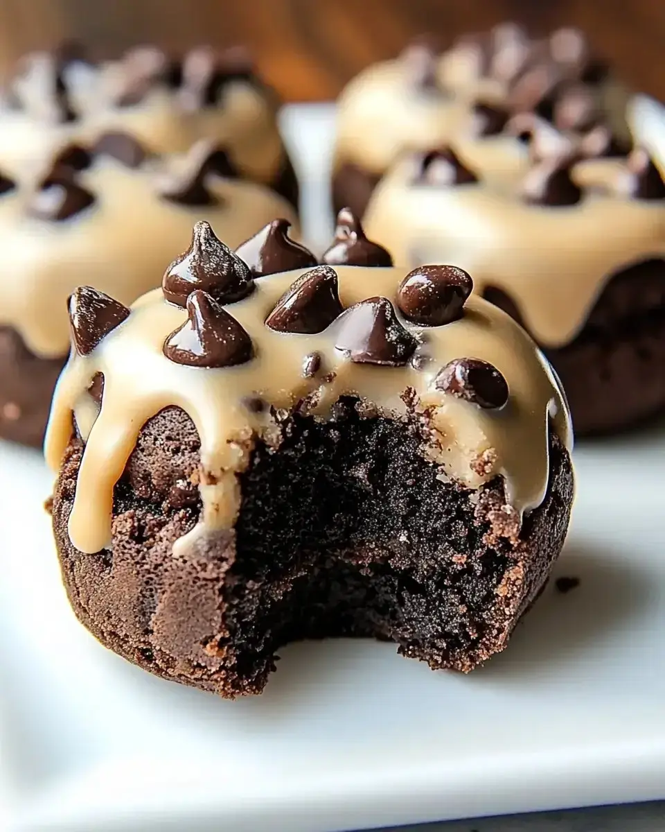 A close-up image of chocolate muffins with caramel icing and chocolate chips on top, one muffin showing a bite taken out.