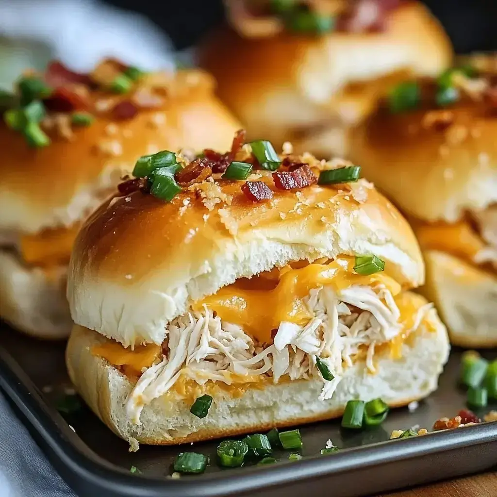 A close-up of a pulled chicken sandwich with melted cheese, topped with green onions and bacon bits, on a tray.