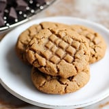 A plate of three freshly baked peanut butter cookies with a crisscross pattern on top.