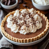 A rich chocolate pie topped with whipped cream and chocolate shavings.